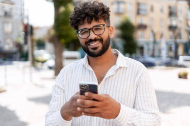 Şehir caddesinde dikilirken cep telefonu kullanan neşeli genç bir işadamının portresi