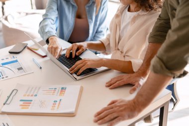 İş arkadaşları bir proje üzerinde işbirliği yapıyorlar. Masada grafikler ve çizelgeler olan bir dizüstü bilgisayardaki verileri analiz ediyorlar. Başarı elde etmek için birlikte çalışıyorlar.