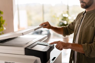 Parlak bir ofiste modern çok işlevli bir yazıcı kullanarak, profesyonel bir ortamda verimlilik ve modern teknoloji sergileyen bir iş adamının belgelerini yakından taraması. Teknoloji konsepti