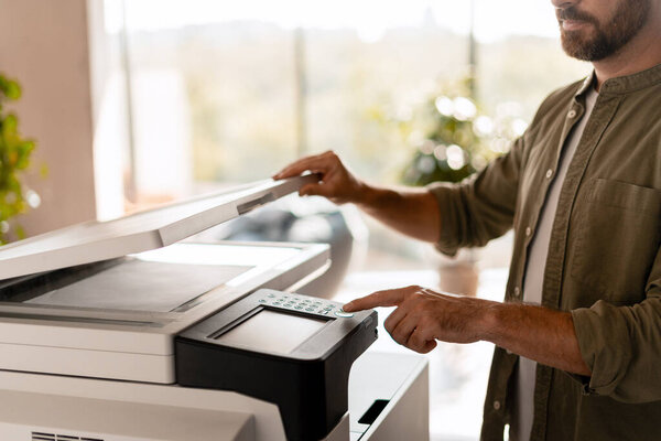 Крупный план бизнесмена, сканирующего документы с помощью современного многофункционального принтера в ярком офисе, демонстрирующего эффективность и современные технологии в профессиональной обстановке. Технологическая концепция