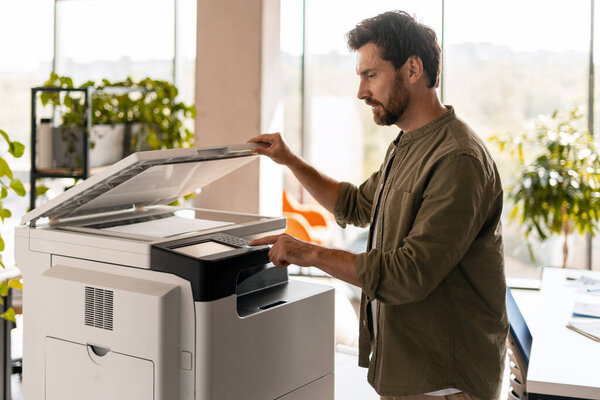 Работник офиса, работающий на многофункциональном принтере, выделяет современные офисные технологии и эффективность рабочего процесса в ярком, заполненном работой рабочем пространстве. Концепция работы офиса