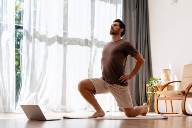 Yakışıklı, sakallı, laptopla içeride yoga egzersizi yapan bir İspanyol. Çevrimiçi eğitim, egzersiz konsepti