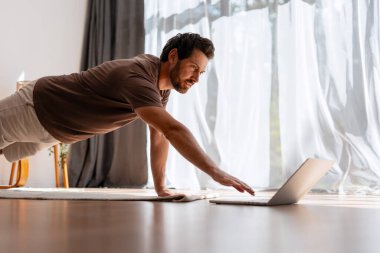 Yakışıklı, orta yaşlı adam evde antrenman yapıyor. İnternetteki spor rehberliği tahtada duruyor. Çevrimiçi eğitim kavramı