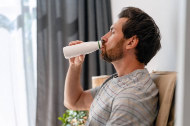 Rahatlamış, orta yaşlı, sakallı bir adam, sakin bir şekilde, fotokopi odasının içinde ferahlatıcı içkinin tadını çıkarıyor. Sağlıklı yaşam tarzı, reklam konsepti