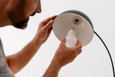 Sakallı adam enerji tasarrufu yaparak ampulü modern lamba armatürüne takıyor. Onarım, ev konsepti