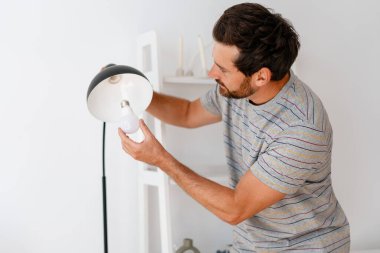Sakallı Latin adam, tamirci lambadaki ampulü değiştirerek ev ışıklandırmasını tamir ediyor. Tamir, elektrik konsepti