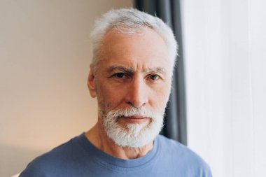 Beyaz saçlı ve sakallı olgun bir adam kameraya bakarak ciddi, kendinden emin ve erkeksi bir ifade yakalıyor.