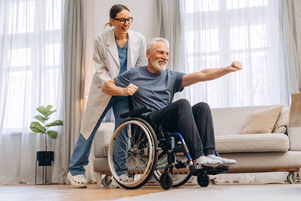 Caregiver assisting a cheerful senior man in a wheelchair doing arm exercises, supporting rehabilitation at home