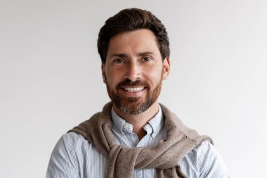 Gülümseyen sakallı, şık, sıradan kıyafetler giyen, kendine güvenen ve kameraya bakarak mutlu bir Latin. Dost canlısı iş adamı beyaz arka planda yalnız poz veriyor. Reklam kavramı