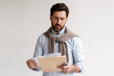 Odaklanmış sakallı işadamı, beyaz arka planda izole bir şekilde duran panodaki belgeleri okuyor. Ciddi sakallı adam çalışıyor. İş konsepti