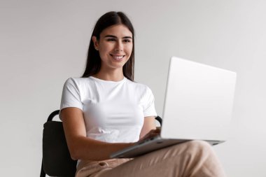 Uzaktan kumanda için dizüstü bilgisayar kullanan, rahat koltukta oturan neşeli bir kadın. Beyaz arka planda izole edilmiş klavyede daktilo yazan profesyonel bir iş kadını. Çevrimiçi teknoloji kavramı