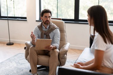 Genç bir kadın hastaya danışmanlık yapan erkek psikolog, akıl sağlığı sorunlarını tartışıyor ve modern bir ofiste terapi seansında destek öneriyor. Tedavi kavramı