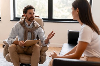 Modern ofisteki rahat koltukta oturan erkek psikolog terapi sırasında kadın hastaya danışmanlık yapıyor. Zihinsel yardım kavramı