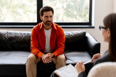 Modern ofiste terapi seansı sırasında orta yaşlı bir adam psikologla konuşuyor. Normal kırmızı gömlek giyen yakışıklı bir erkek hasta. Metal sağlık konsepti