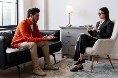 Üzgün, sakallı, orta yaşlı bir adam ofiste terapi görüyor, psikologla konuşuyor. Neşeli kadın, günlük kıyafet giyen doktor oturuyor ve dinliyor. Ruh sağlığı konsepti