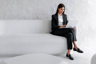 Ciddi bir iş kadını resmi giysiler giyip evde dizüstü bilgisayarla çalışıyor. Serbest çalışan kadın, klavyede yazan metin yazarı, kopyalama alanı. Çevrimiçi teknoloji kavramı