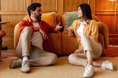 Mutlu çift evde dinleniyor, sohbet ediyor, gülümseyen adam ve kadın yerde oturuyor. Aşk, rahatlatıcı konsept