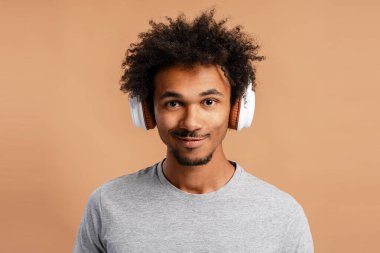 Beyaz kulaklıklı, gri tişörtlü genç bir Afro-Amerikalı sıcak bir arka planda müzik dinliyor.