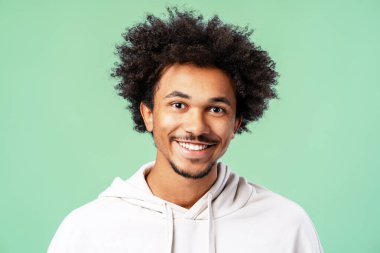 Afro saçlı ve sakallı genç bir adam mutlu bir şekilde gülümsüyor. Nane yeşili arka planda mutluluk ve pozitifliği resmediyor.