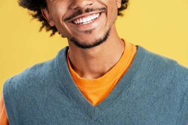 Mutlu genç siyah adam geniş bir gülümseme, parlak sarı bir arka plan karşısında temiz beyaz dişler gösteriyor, sevinç ifade ediyor