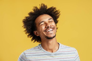 Mutlu siyah adam eğlence ve neşe buluyor gözleri kapalı ve saçlarını kestiriyor, sarı arka planda duruyor.