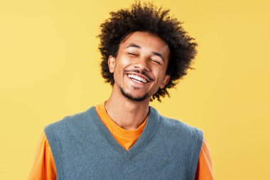 Afro saçlı genç bir adam. Gözleri kapalı gülüyor ve gülümsüyor. Sarı arka planda neşe ve mutluluğu ifade ediyor.