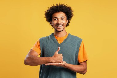 Afro saçlı mutlu genç adam gülümsüyor, baş parmak işareti yapıyor ve fotokopi alanı için açık bir el hareketi yapıyor.