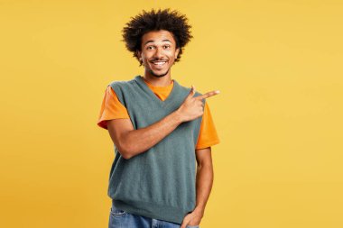 Genç adam gülümsüyor ve parmaklarını sağa doğru gösteriyor, yön gösteriyor ya da sarı arka planda kopya alanı olan tavsiyelerde bulunuyor