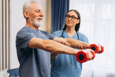 Oturma odasında elinde dambıllar olan hemşire ile fizyoterapi yapıyor. Olgun bir hasta, doktorla birlikte çalışıyor. Sağlık hizmeti kavramı