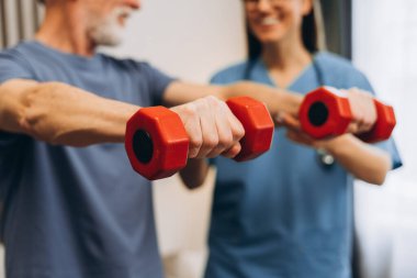 Üst düzey bir adam hemşire ile rehabilitasyon egzersizleri yapıyor. Yakın çekime odaklanıyor. Modern klinikte gülümseyen mutlu doktor ve erkek hasta eğitimi. Sağlık hizmeti kavramı