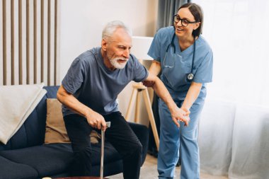Hemşire yaşlı bir adama bastonla yardım ediyor, gülümseyen bir rehabilitasyon uzmanı olgun bir hastaya yardım ediyor. Sağlık hizmetleri, destek kavramı