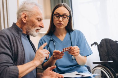 Uzman hemşire, evdeki modern oturma odasında otururken ihtiyara ilacı açıklıyor. Danışmanlık, tedavi kavramı