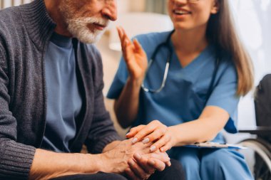 Hemşire, yaşlı bir hastanın elini tutan güzel bir kadın sıcak oturma odasında oturuyor seçici bir odak noktası, yakın çekim. Destek, yardım kavramı