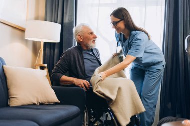 Mutlu, gülümseyen bir kadın, tekerlekli sandalyedeki yaşlı adamı destekleyen bir hemşire. Destek, sağlık hizmeti kavramı