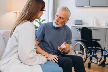 Kadın doktor ev ziyareti sırasında kıdemli adama danışıyor. Hemşire ve yetişkin hasta oturma odasında oturuyor. Sağlık hizmeti kavramı