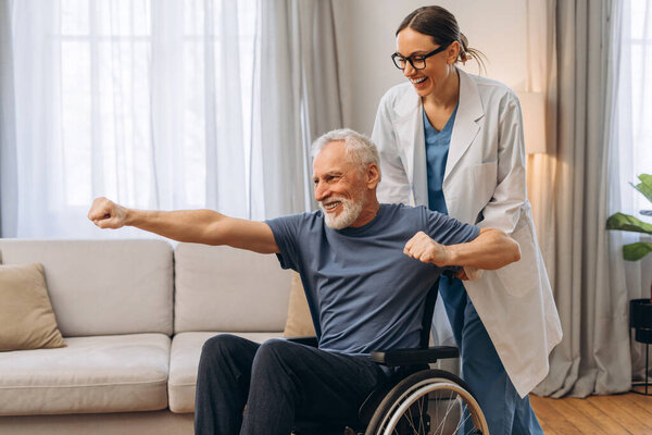 Caregiver assisting senior man in wheelchair during rehabilitation. Mature patient exercising in modern clinic. Health care concept