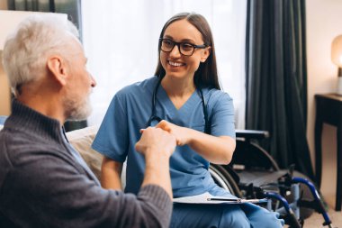 Gülümseyen kadın hemşire ve yaşlı hasta yumruğu modern klinikte destek için çarpışıyor. Mutlu doktor ve kıdemli adam konuşuyor. Destek, sağlık hizmeti kavramı