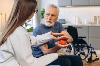 Kadın bakıcı, kıdemli adama el egzersizlerinde yardım ediyor, evde eğitim görüyor. Profesyonel hemşire evde olgun bir hastaya yardım ediyor. Rehabilitasyon kavramı