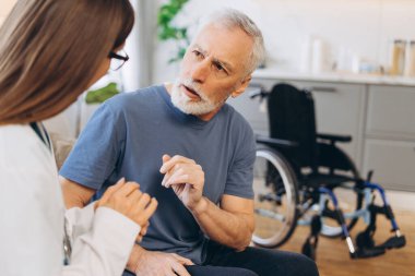 Kadın doktor, evdeki tekerlekli sandalyedeki yaşlı adama danışıyor. Profesyonel hemşire yaşlı bir hastayla konuşuyor. İletişim, sağlık hizmeti kavramı