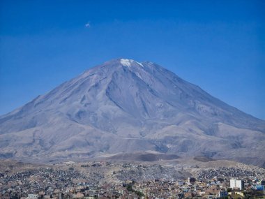 Arkaplanı dağ sıraları ve volkanlardan oluşan birçok ağacı olan bir şehir.