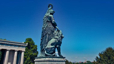 Kamu parkının ortasında bronz bir kadın ve aslan heykeli.