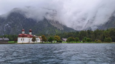 Göle bakan bir ev, orman dağlarının yanında ve sisli bir sürü bulut.
