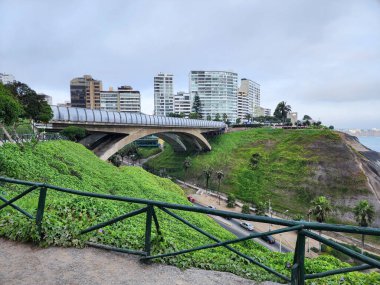 Kayalıkların ve yeşil bahçelerin yanında cam parmaklıkları olan beton bir yaya köprüsü manzarası