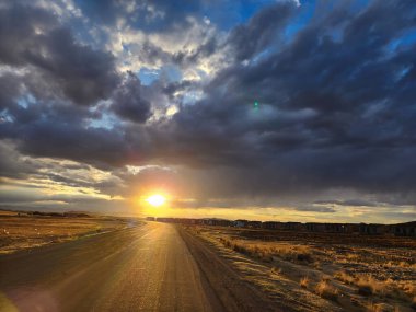 Yol kenarında gün batımı ve sarı çimenli çayırlar.