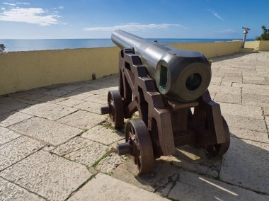 Demir Top, mavi gökyüzüyle Engin Okyanus Ufkunu işaret ediyor. Demir tekerlekler üzerinde tarihi top.