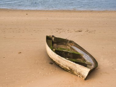 Low Tide 'da Sandy Sahili' nde demirli bir eski kayık. Pas ile süslenmiş yıpranmış eski bir tekne, alçak gelgit sırasında sakin bir kumsalın yumuşak kumlarında zarif bir şekilde demirler..