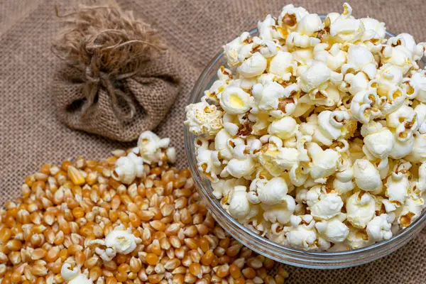 Bowl of popcorn on burlap table in rustic style with corn seeds, eco snack concept
