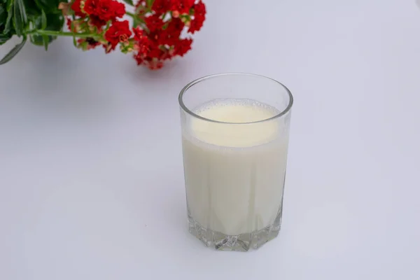 Glas Milch Auf Weißem Hintergrund Mit Roter Blume Dahinter — Stockfoto