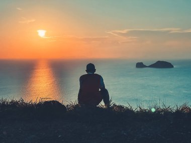 Man watching colorful tropical sunset. Back view silhouette against sea water and orange sky with sun and clouds. Amazing natural summer scenery. Travel, tourism, holiday, relax in Thailand island