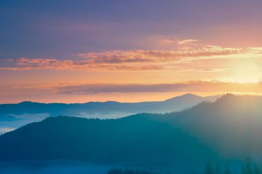 Yumuşak ışıkta renkli dağ gündoğumu. Mavi dağ sırası turuncu ve pembe gökyüzüne karşı. Highland Valley 'de sabah sisi ve çam ağacı ormanı. Güzel doğa yaz manzarası. Seyahat arkaplanı